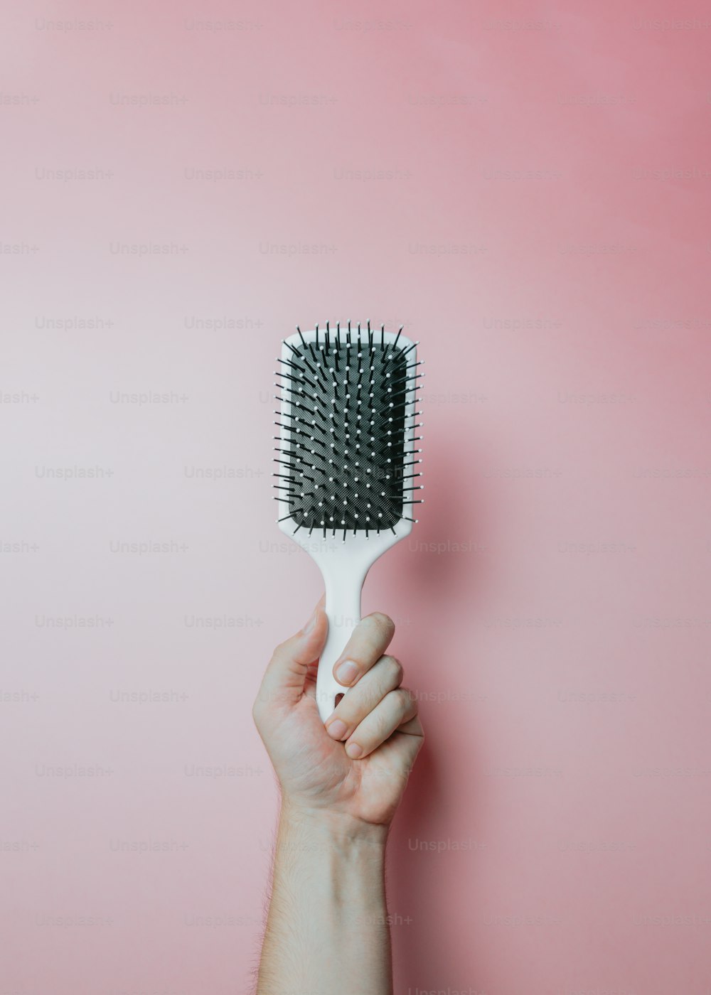 La mano de una mujer sosteniendo un cepillo para el cabello sobre un fondo rosa