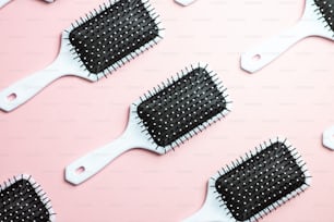 a bunch of black and white hair brushes on a pink background