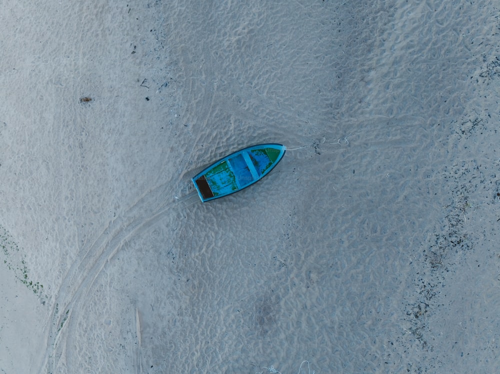 Un petit bateau bleu assis au sommet d’une plage de sable