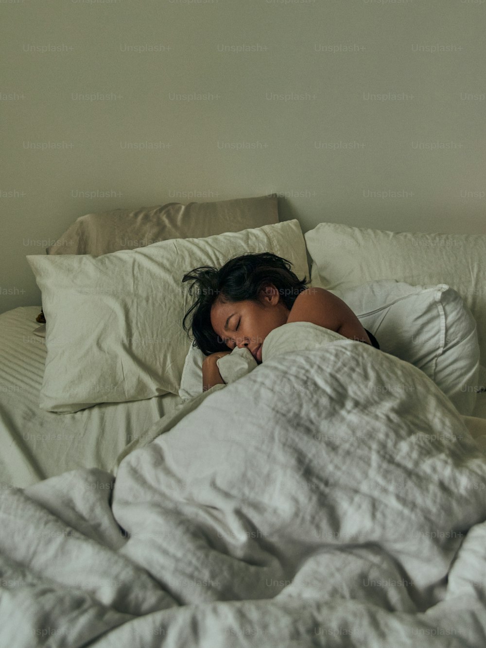 a woman sleeping in a bed with white sheets