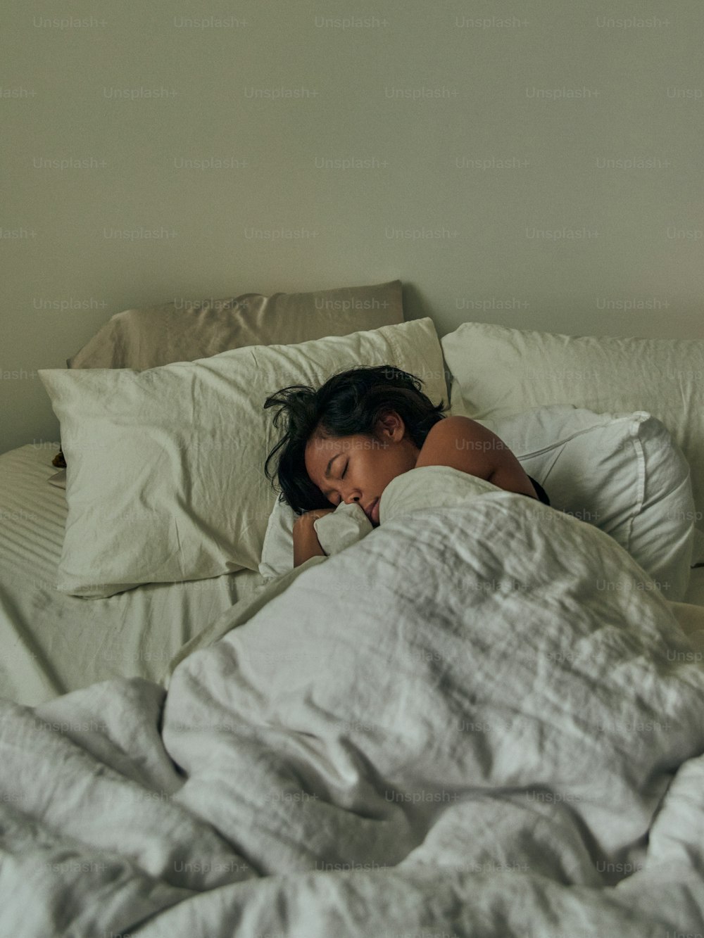 uma mulher dormindo em uma cama com lençóis brancos