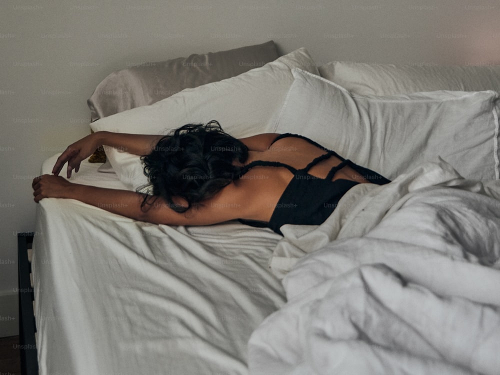 a woman laying on a bed with white sheets