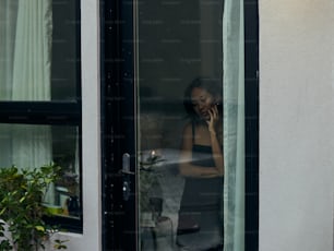 Una mujer hablando por teléfono celular mientras está parada frente a una ventana