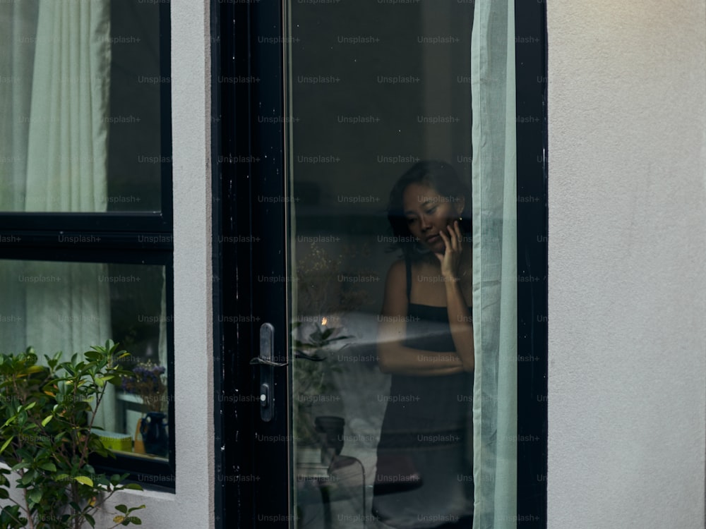 a woman talking on a cell phone while standing in front of a window