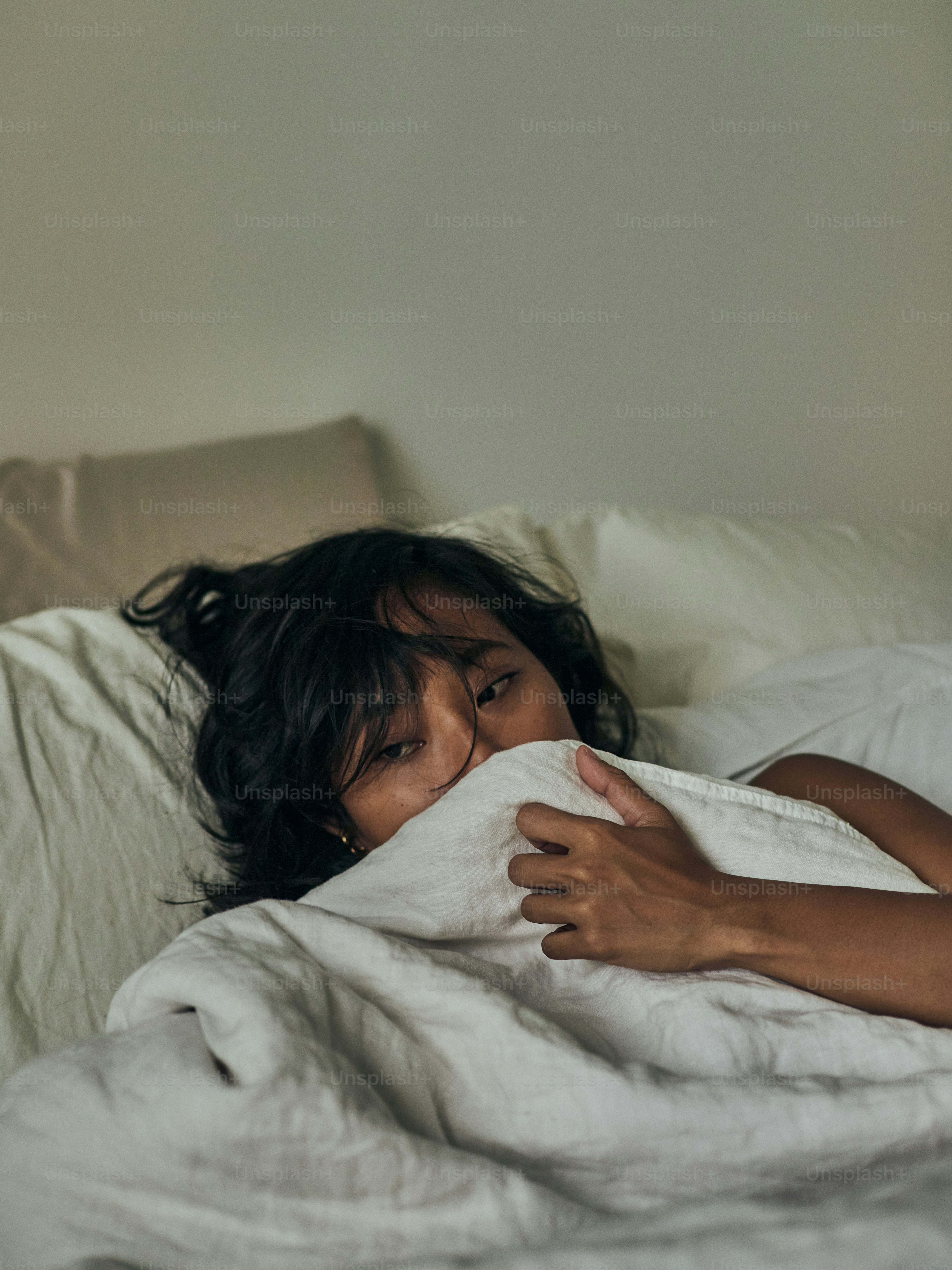 a little girl laying in bed with a white blanket