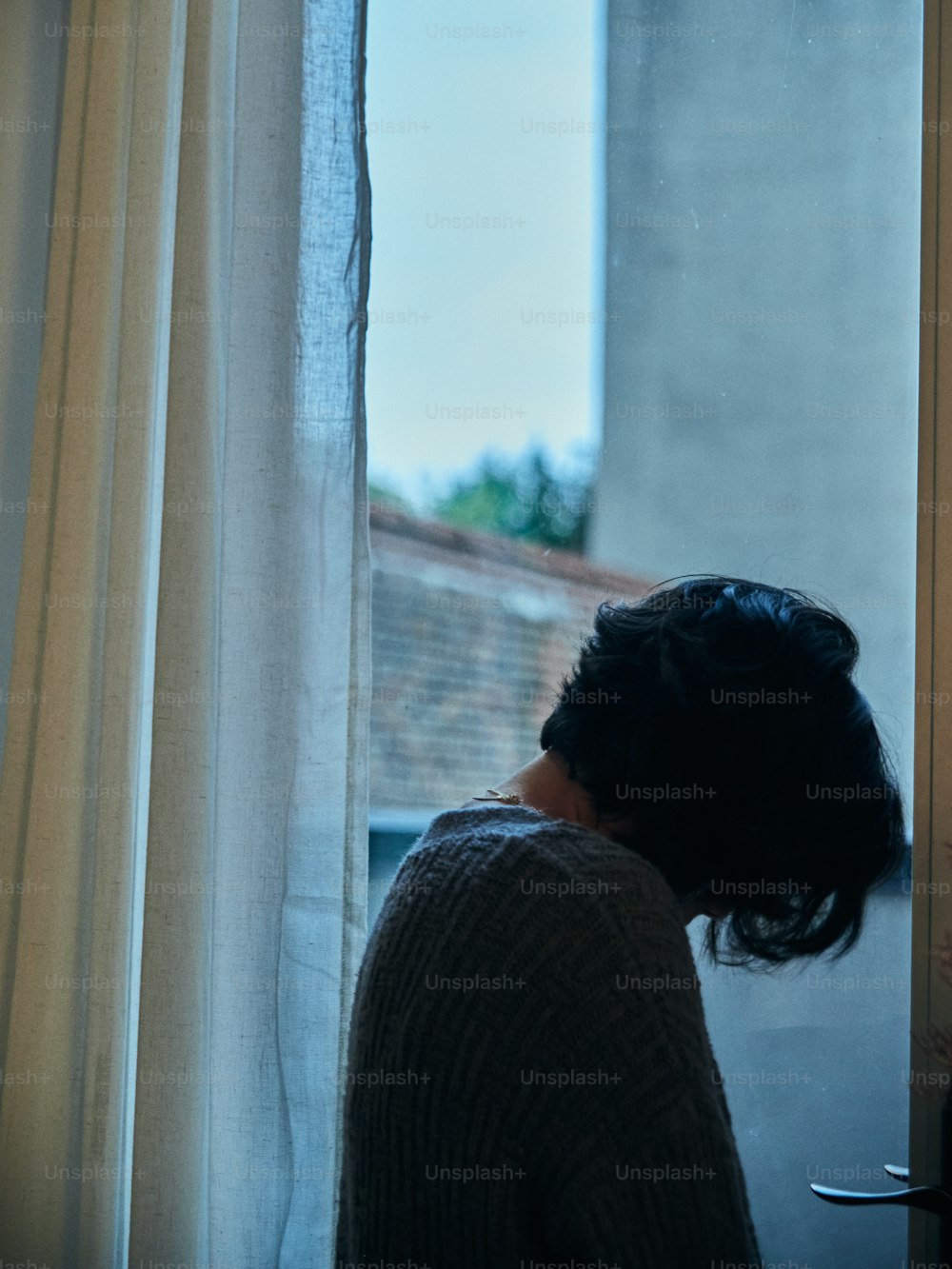 Une femme regardant par une fenêtre un immeuble