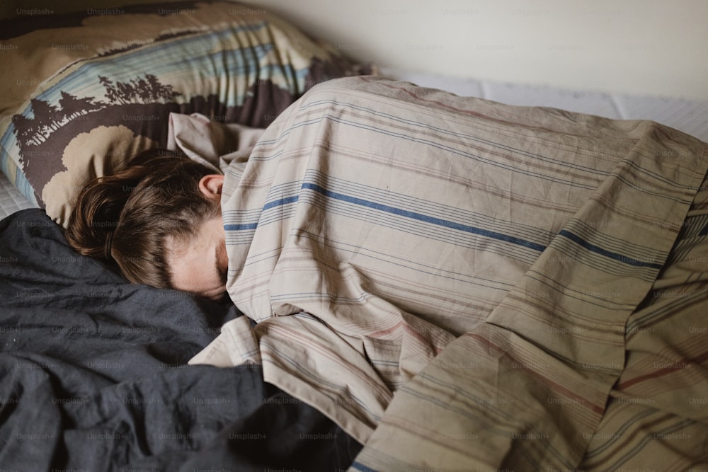 uma jovem que dorme em uma cama sob um cobertor