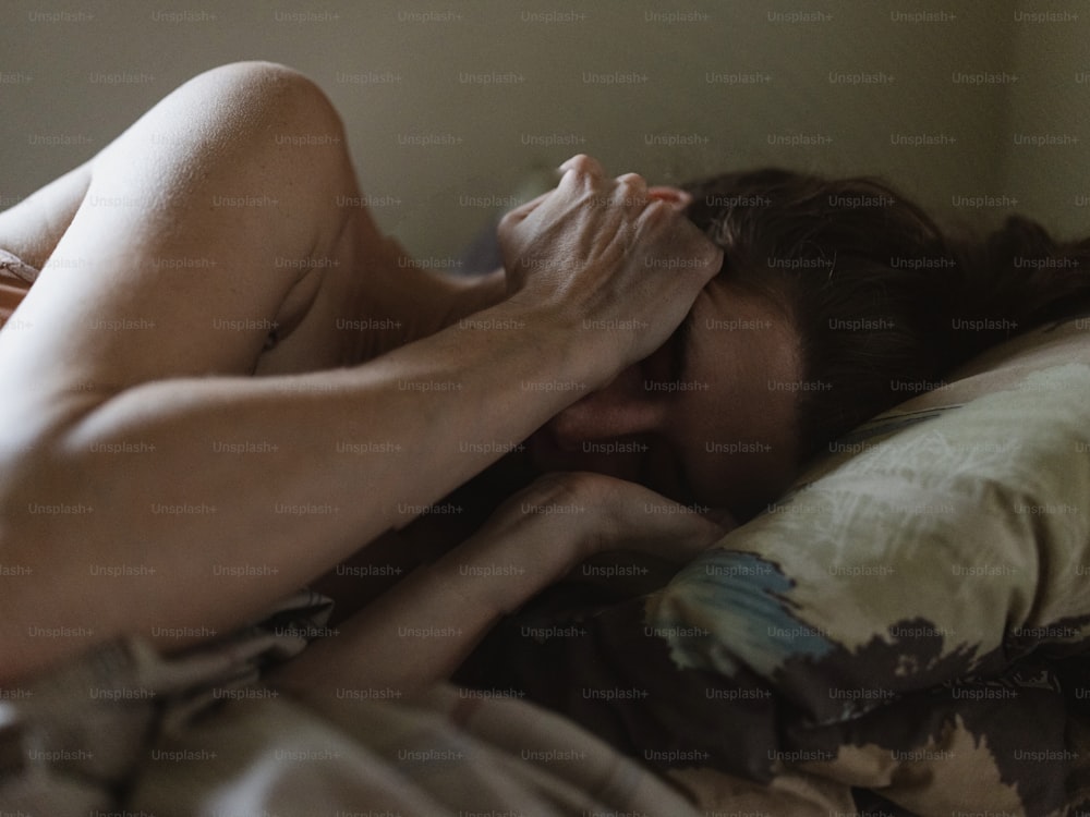uma mulher nua deitada na cama com a cabeça nas mãos
