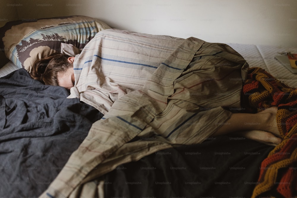 eine Person, die in einem Bett mit einer Decke schläft