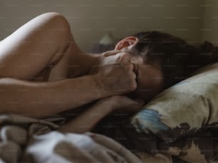 枕の上に頭を乗せてベッドに横たわる裸の女性