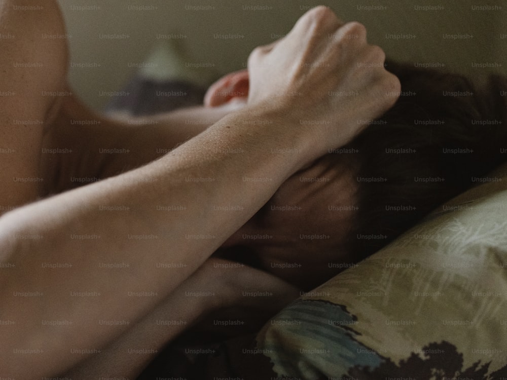Un uomo a torso nudo sdraiato su un letto con le mani sulla testa