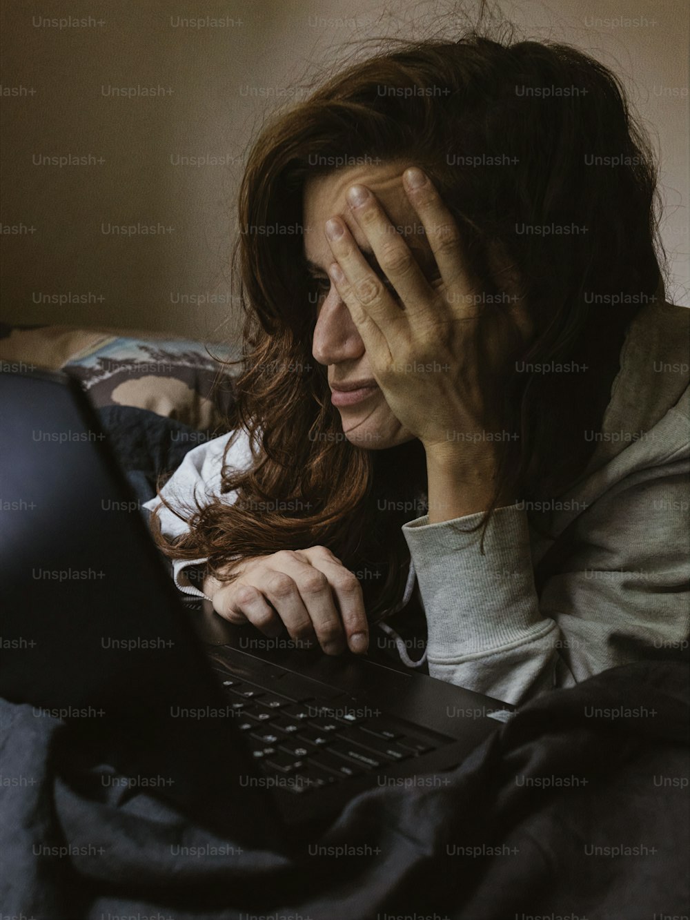 a woman covers her eyes while using a laptop