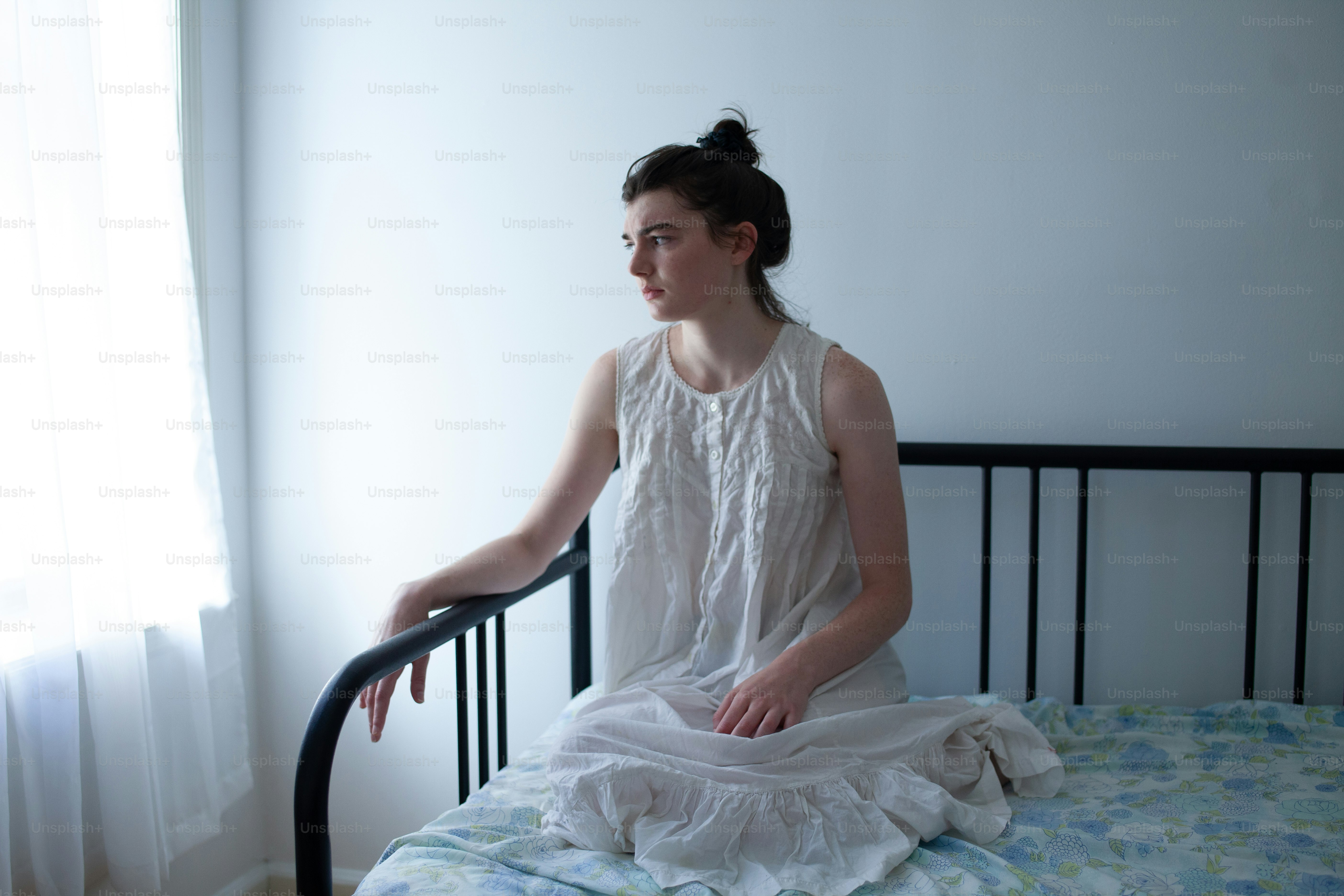 a woman sitting on a bed in a white dress