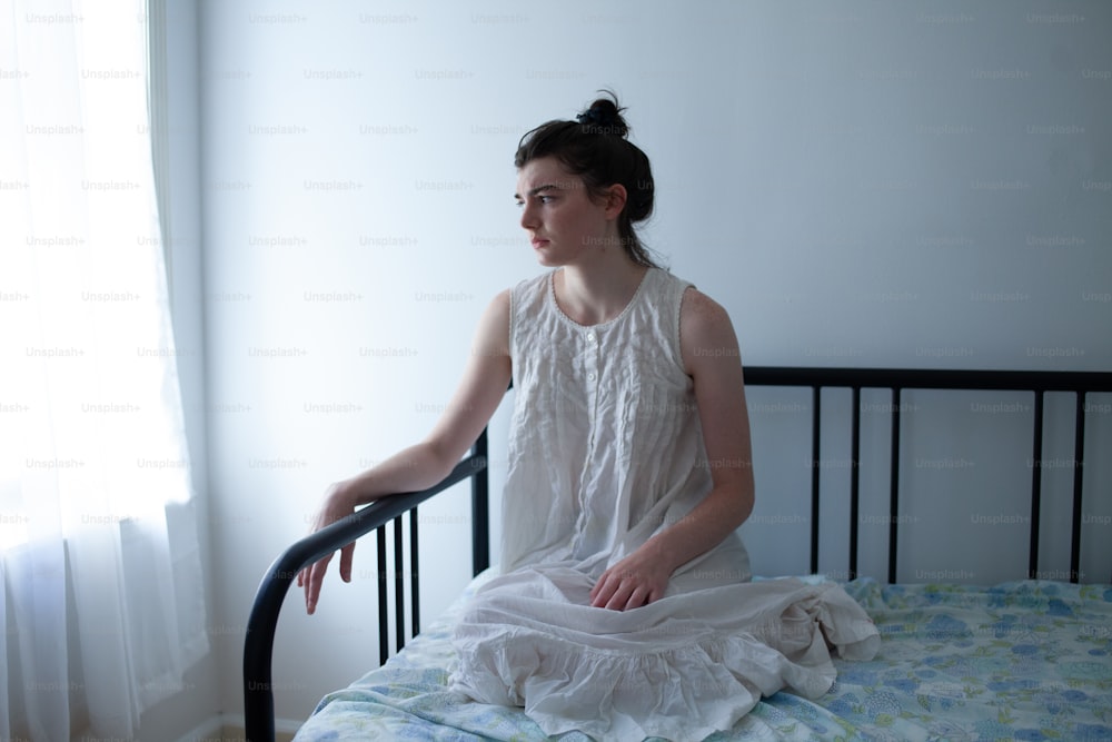 Una mujer sentada en una cama con un vestido blanco