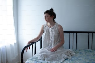 a woman sitting on a bed in a white dress