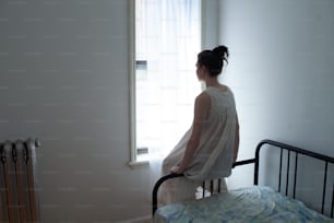 une femme debout sur un lit regardant par une fenêtre