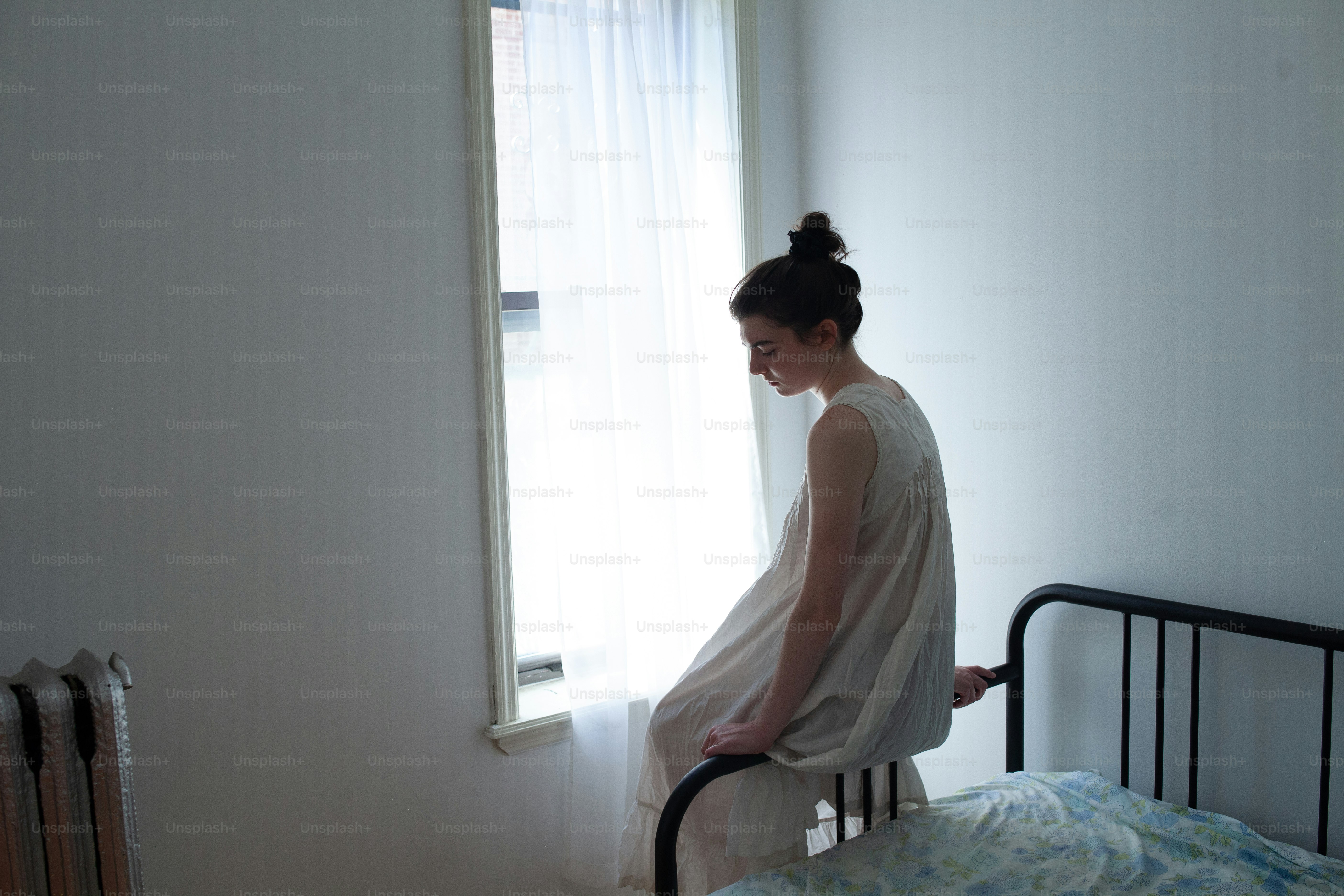 Una mujer sentada encima de una cama junto a una ventana