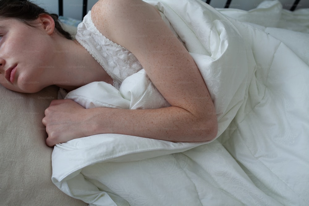 a woman sleeping on a bed with white sheets