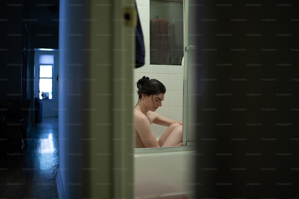 a woman sitting in a bathtub looking at herself in the mirror