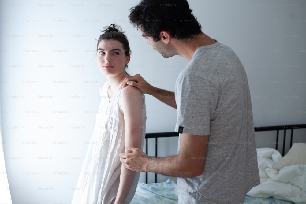 a man fixing a woman's dress in a bedroom