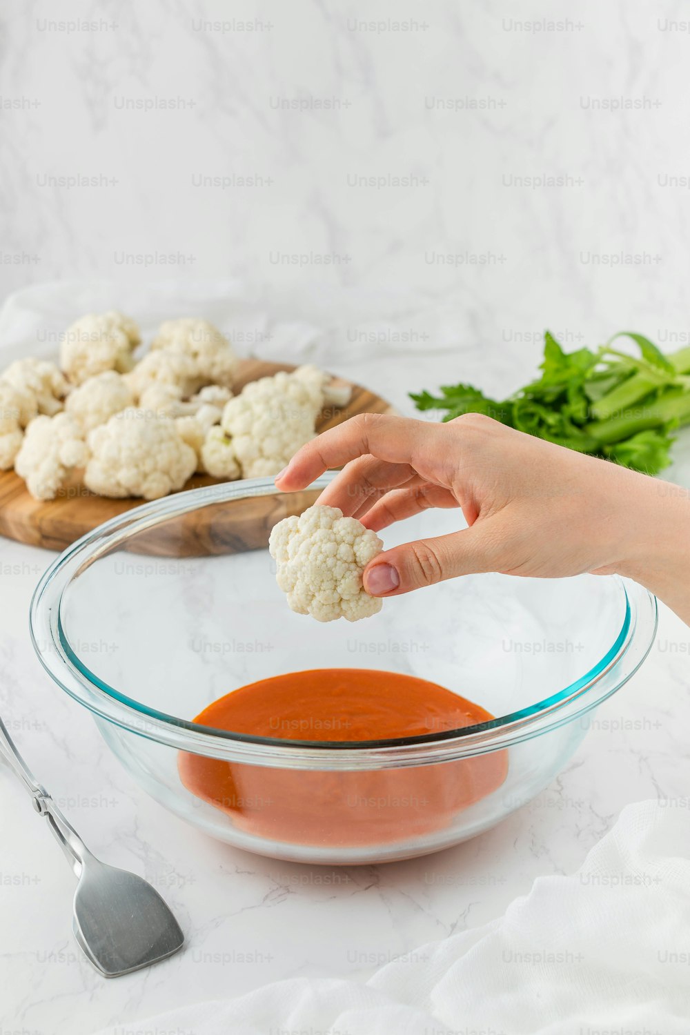 a person dipping sauce into a bowl of cauliflower