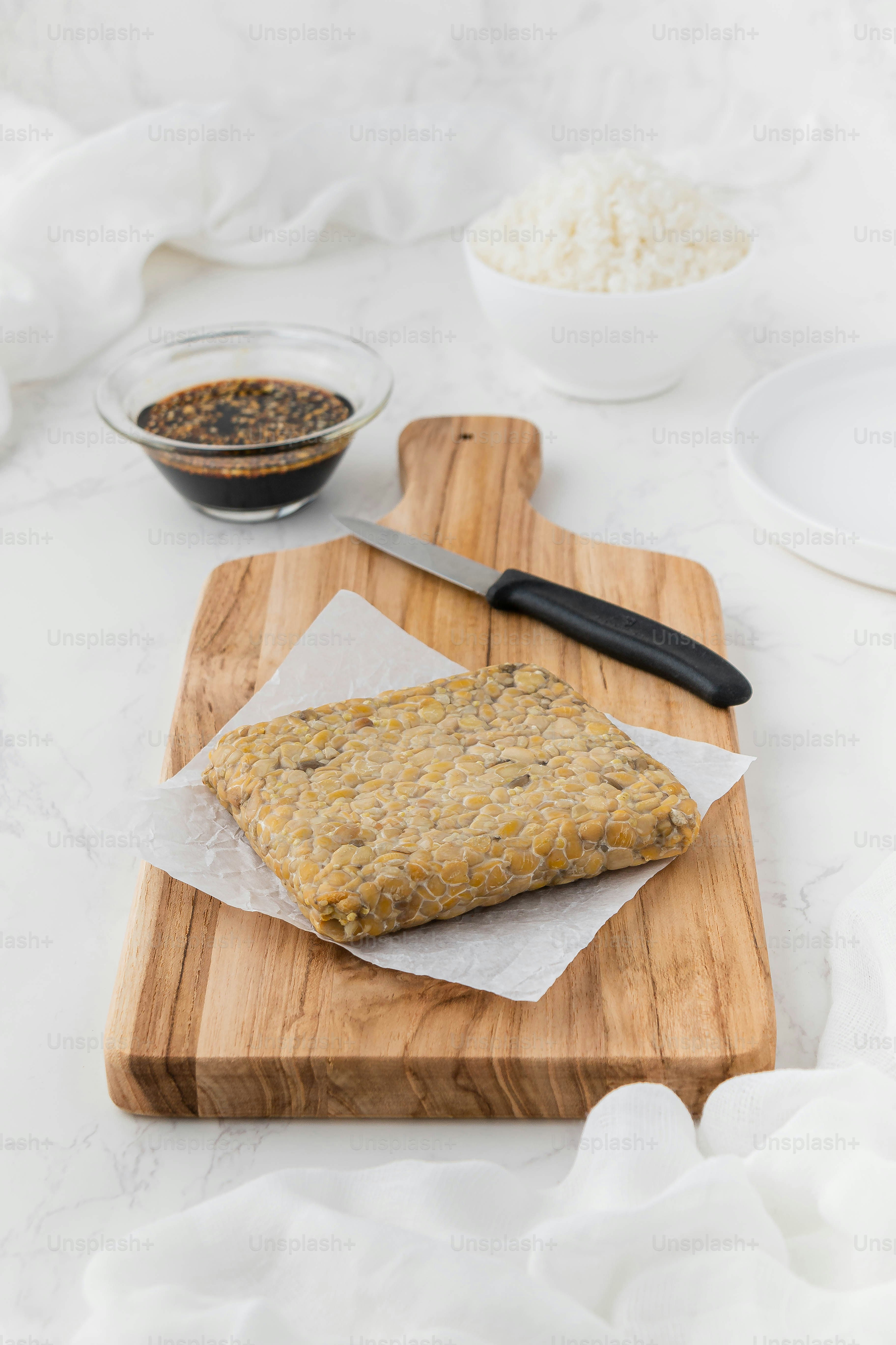 a wooden cutting board topped with food next to a bowl of rice
