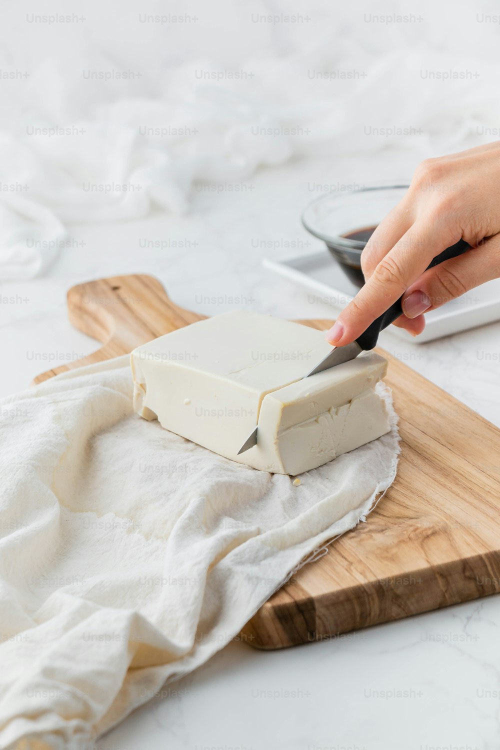a person cutting a block of cheese on a cutting board