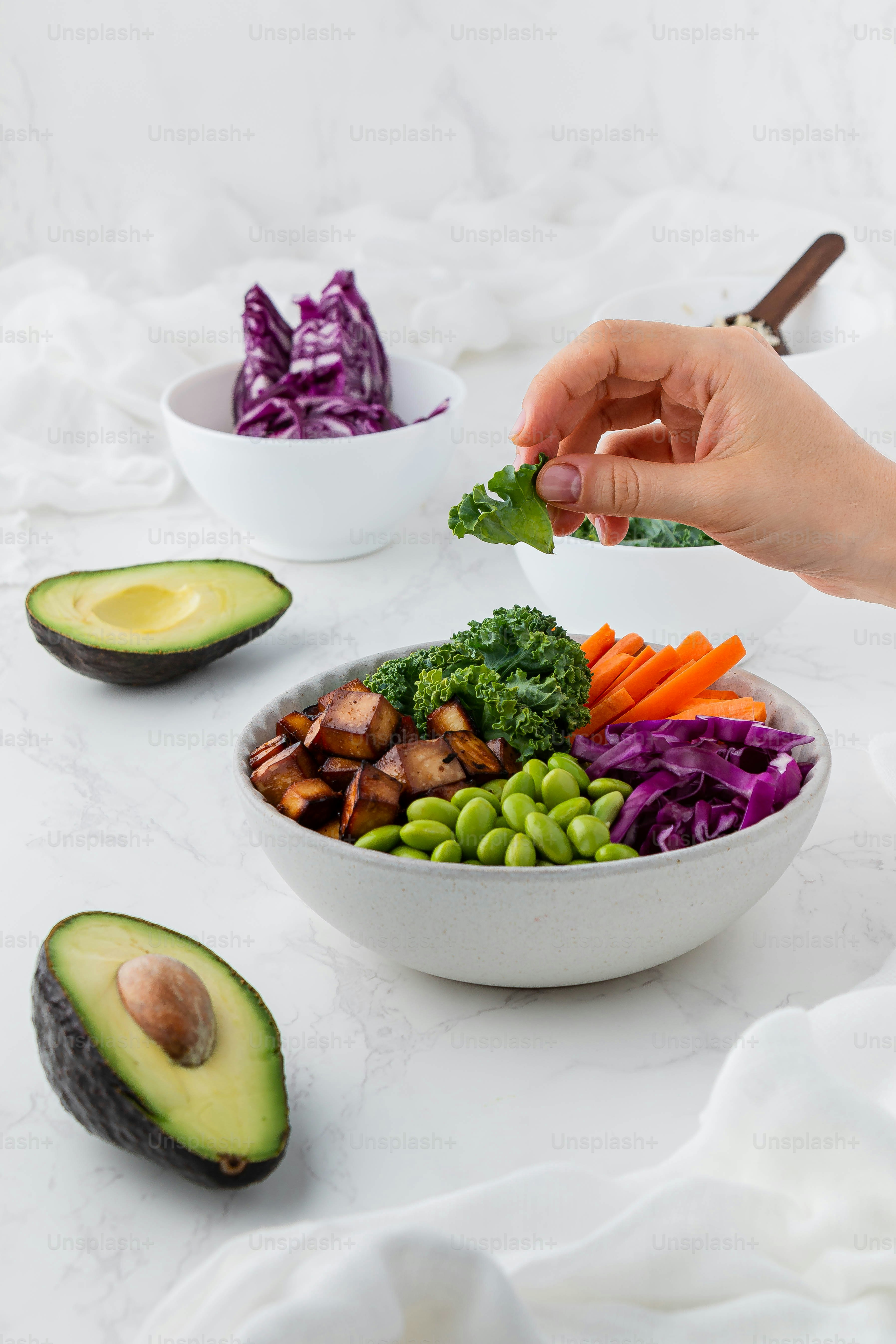 a person holding a piece of broccoli over a bowl of vegetables