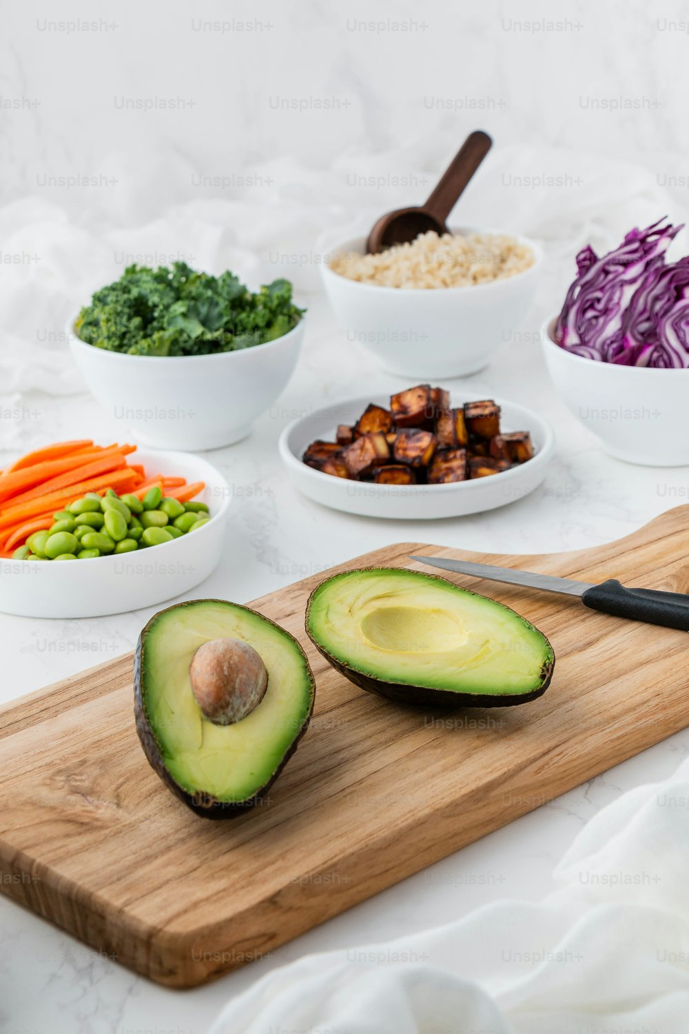 a wooden cutting board topped with sliced avocado next to bowls of vegetables