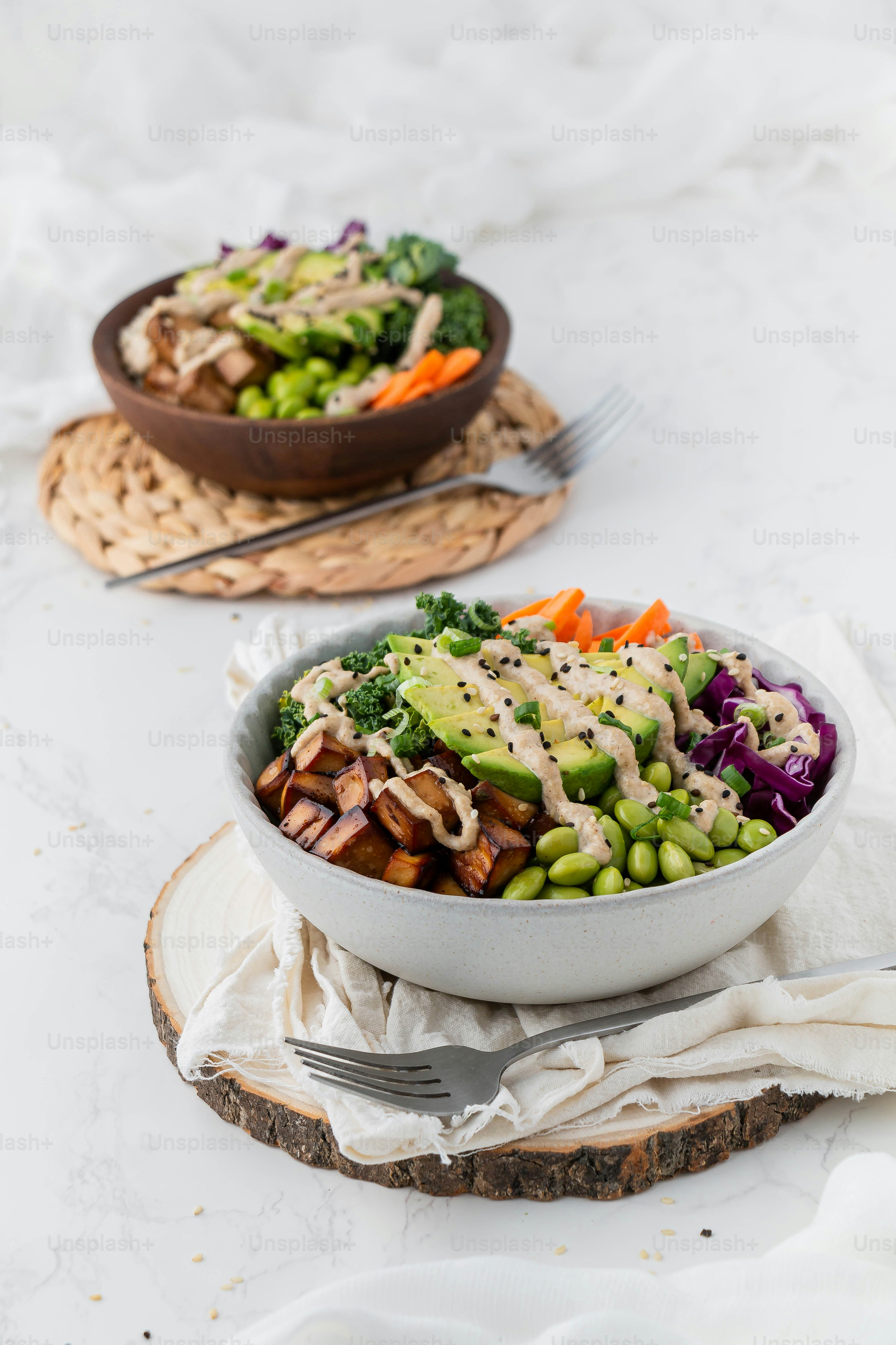 two bowls filled with vegetables and dressing on top of a table