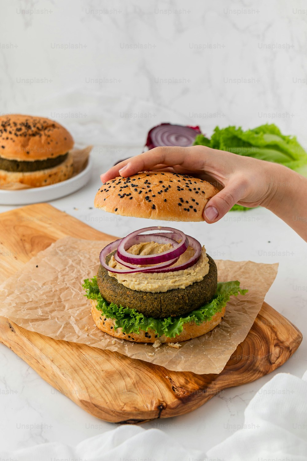 a hand reaching for a hamburger on a cutting board