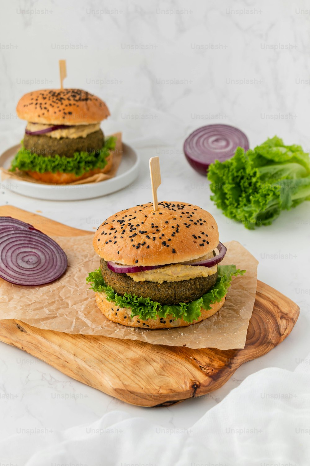 two hamburgers on a cutting board with onions and lettuce