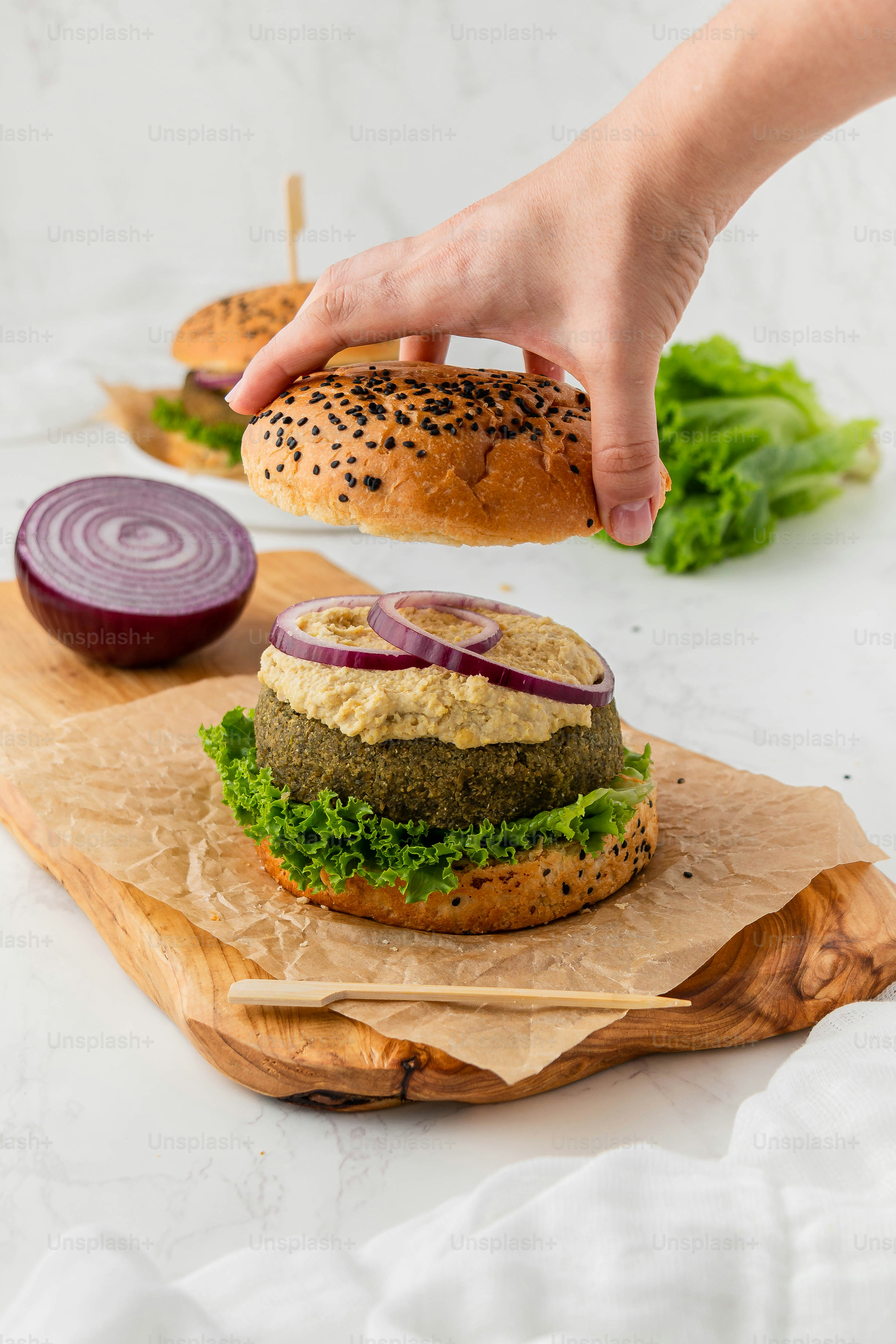 a hand reaching for a burger on a wooden board