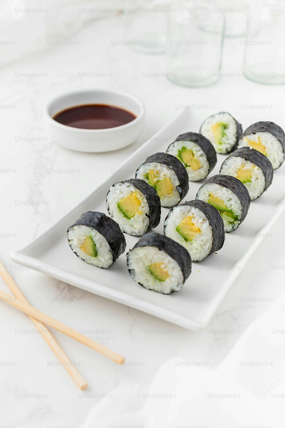 une assiette blanche garnie de sushis à côté d’un bol de sauce