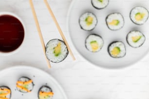 ein Teller Sushi mit Stäbchen neben einer Schüssel Sauce