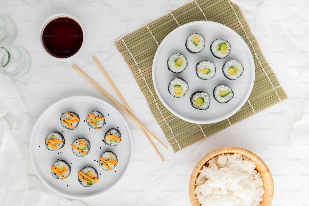um prato de sushi ao lado de uma tigela de arroz e pauzinhos