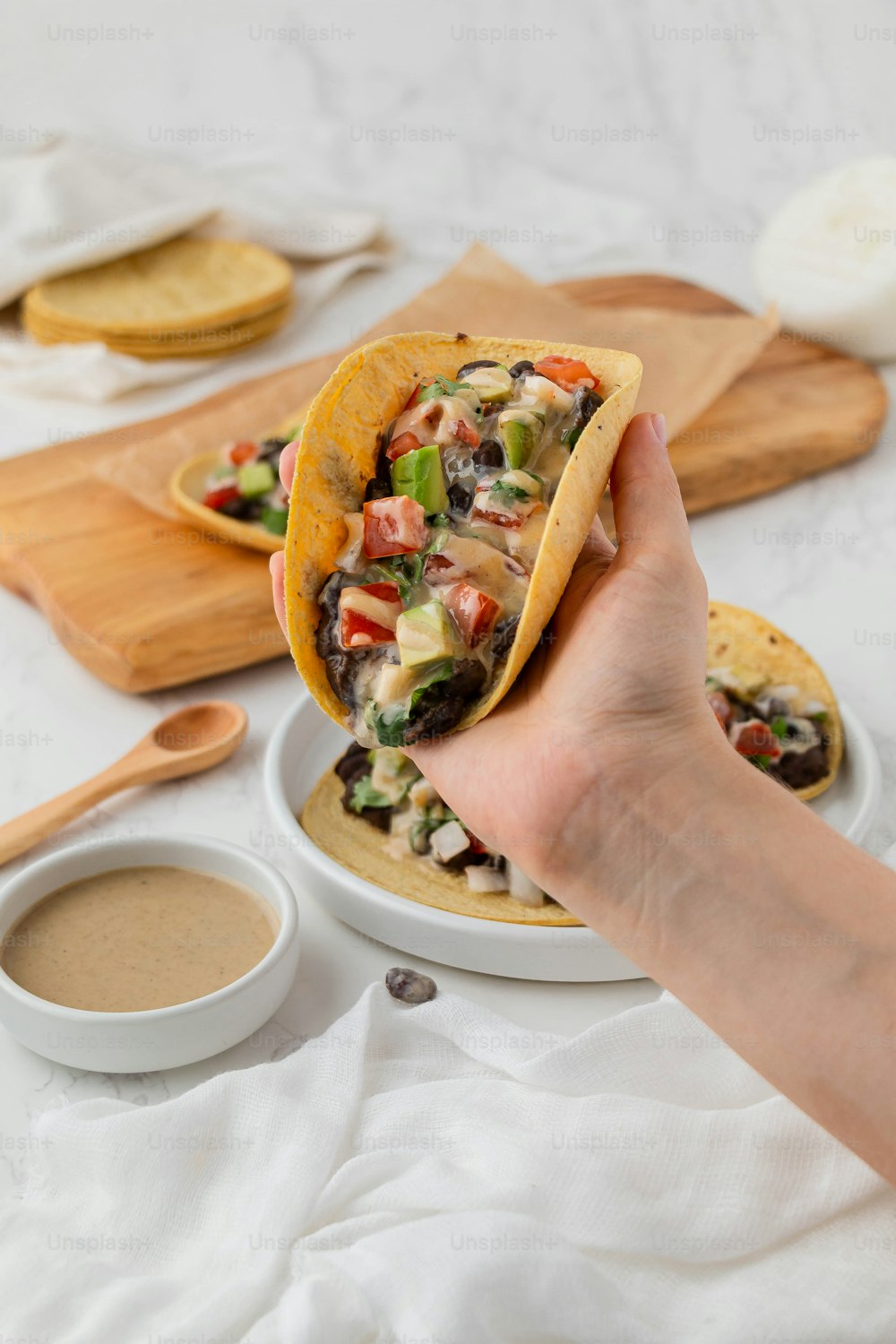 a person holding a tortilla over a plate of food