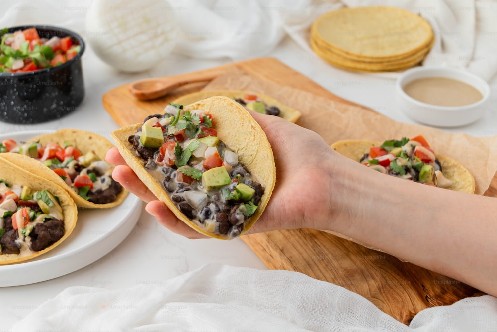 una persona sosteniendo una tortilla rellena de frijoles negros, guacamole