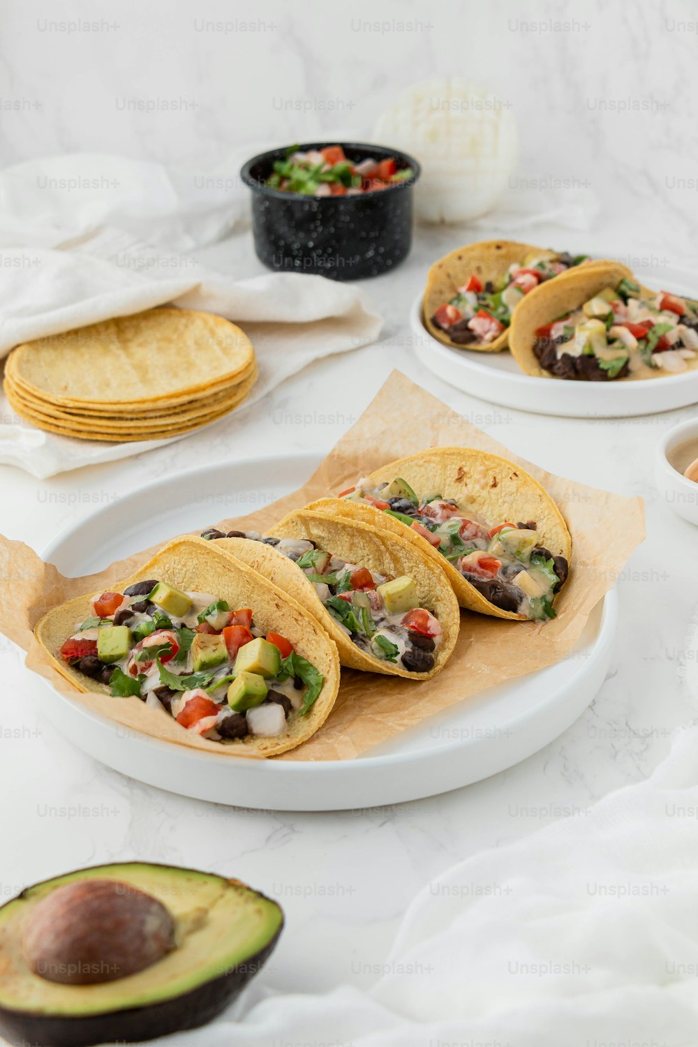 a white plate topped with three tacos next to an avocado