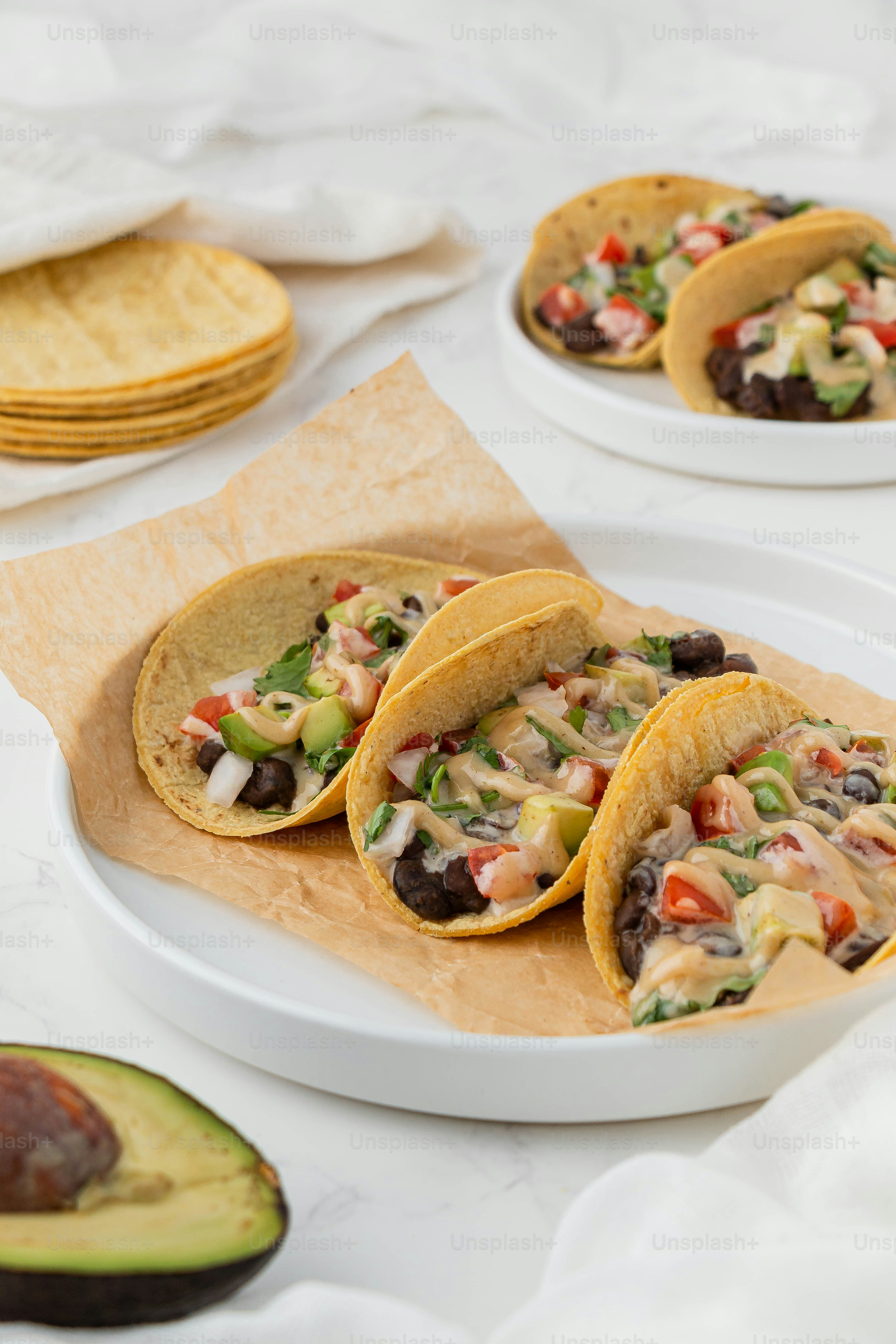 a white plate topped with three tacos next to an avocado