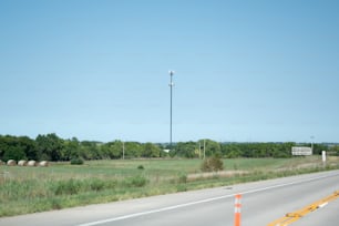 a road with a field of grass and a light pole in the distance