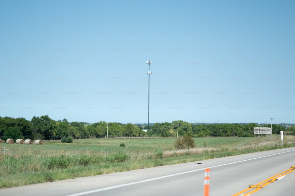 a road with a field of grass and a light pole in the distance