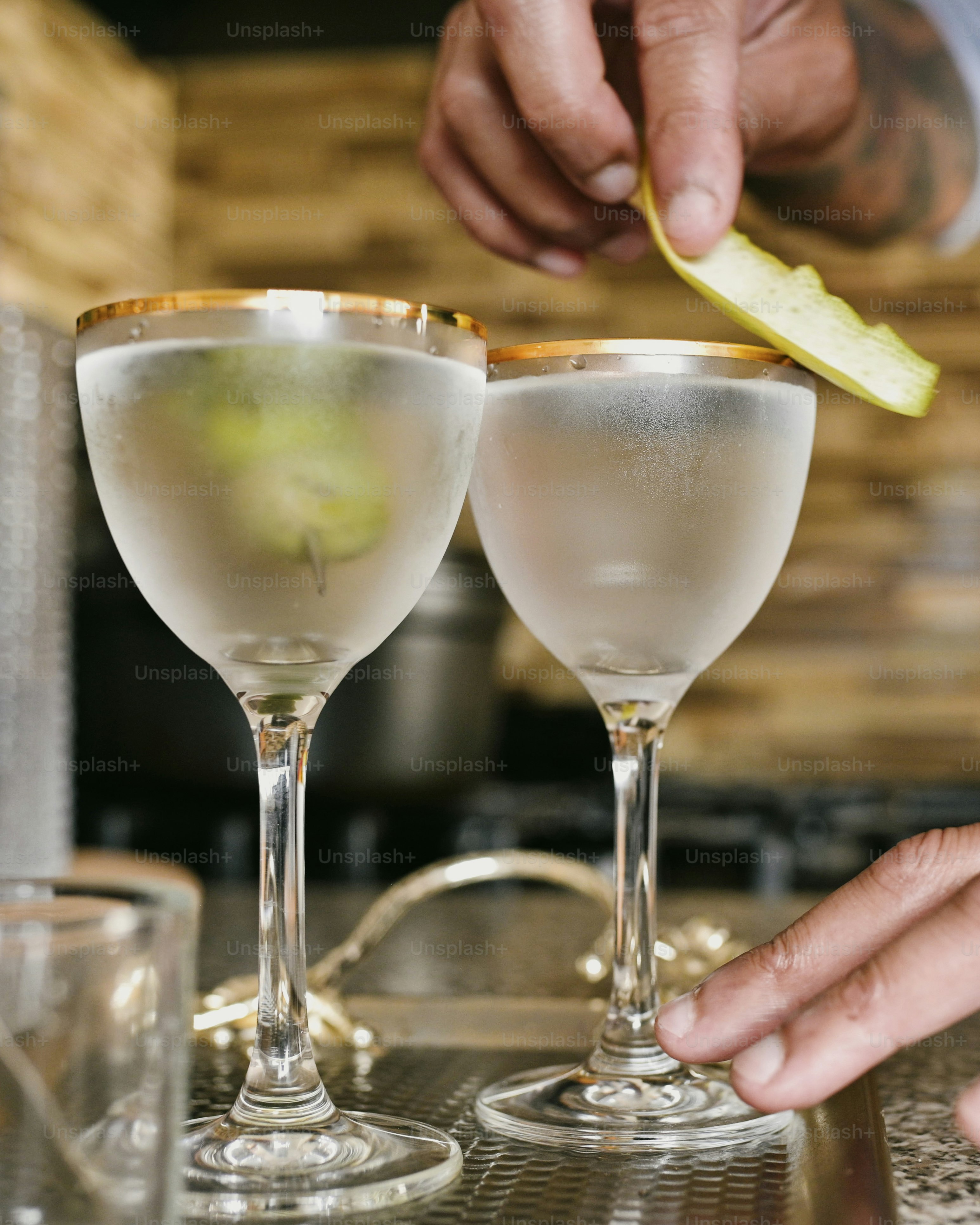 a person is holding a slice of an apple near two glasses of alcohol