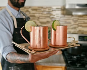 a man holding a tray with two copper mugs