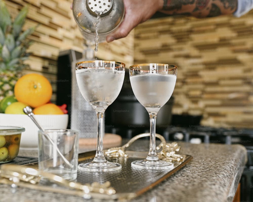 a person pouring a drink into two glasses