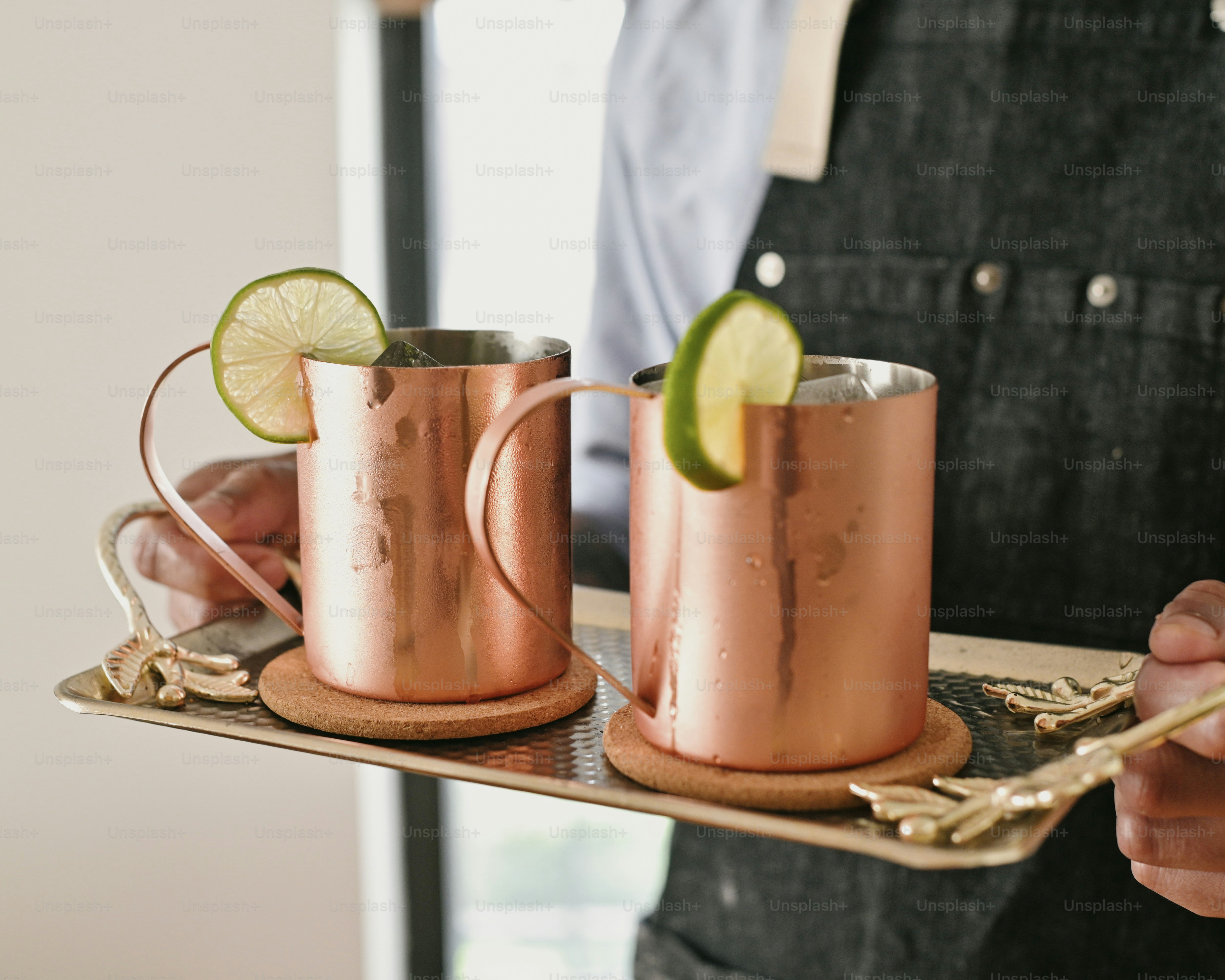a person holding a tray with two copper mugs