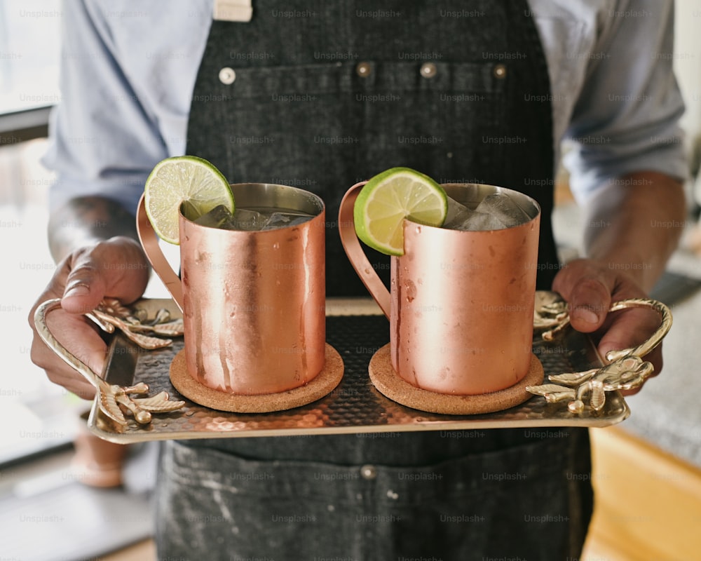 a man holding two copper mugs with lime wedges