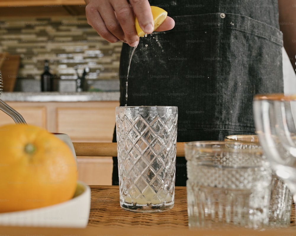 a person in a kitchen squeezing a lemon into a glass