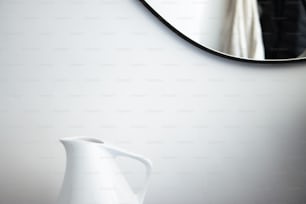 Un jarrón blanco sentado junto a un espejo en una pared