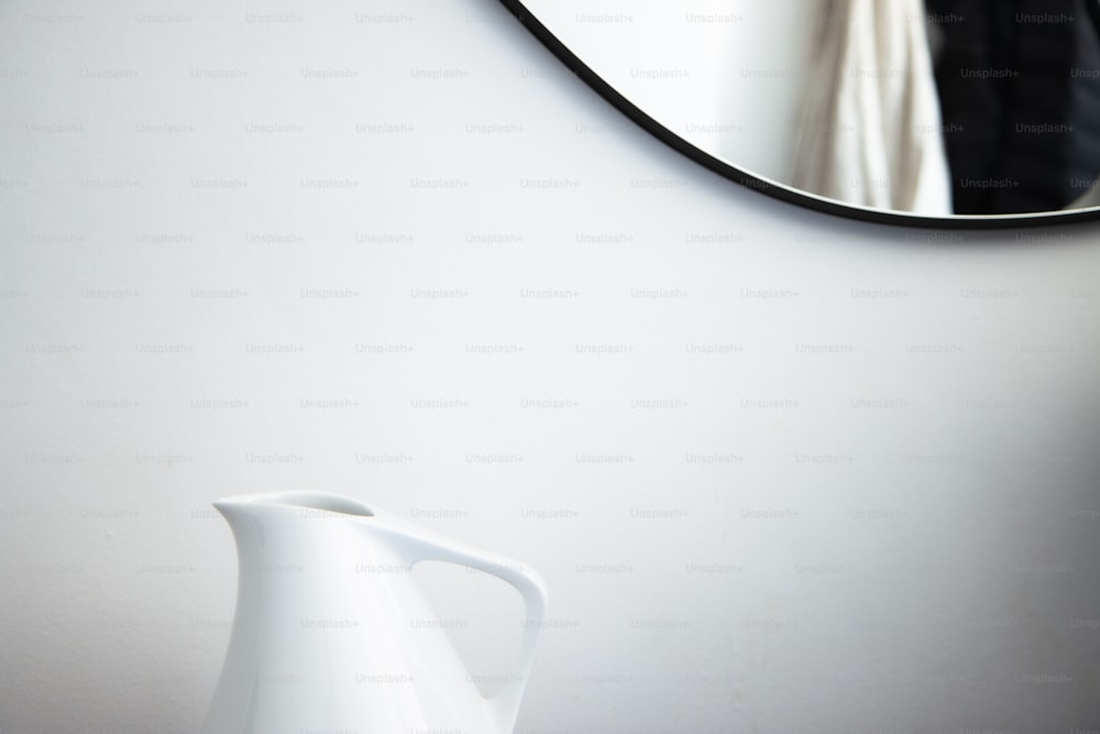 a white vase sitting next to a mirror on a wall